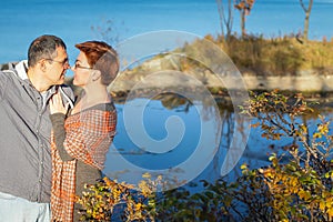 Portrait of loving middle-aged couple in warm clothes hugging in the autumn park at sunset in selective focus