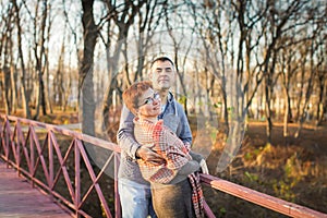 Portrait of loving middle-aged couple in warm clothes hugging in the autumn park at sunset in selective focus