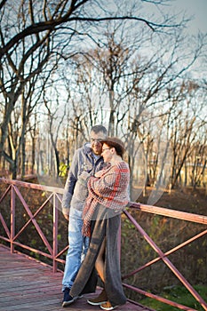 Portrait of loving middle-aged couple in warm clothes hugging in the autumn park at sunset in selective focus