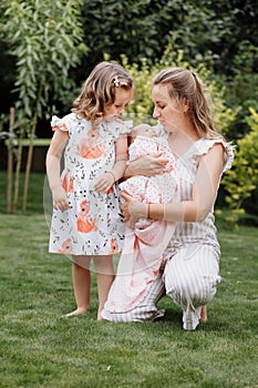 Portrait of loving mother and two adorable kids. little girl and newborn baby girl with mom outdoors on summer day. Happy family