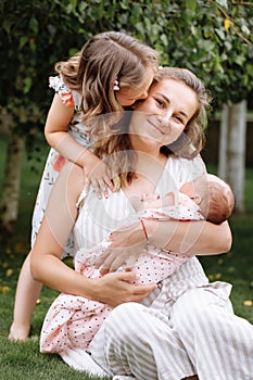 Portrait of loving mother and two adorable kids. little girl and newborn baby girl with mom outdoors on summer day. Happy family