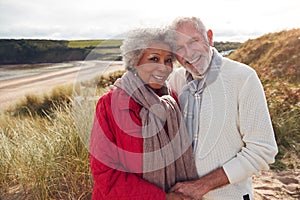 Portrait of Loving Senior Couple Standing And Hugging On Walk In Sand Dunes On Winter Beach Vacation