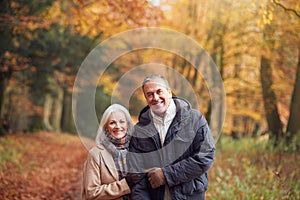 Portrait Of Loving Senior Couple Walking Along Autumn Woodland Path Through Trees