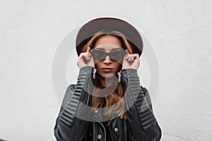 Portrait of luxurious red-haired hipster young woman in dark fashionable sunglasses in purple hat in black stylish leather jacket