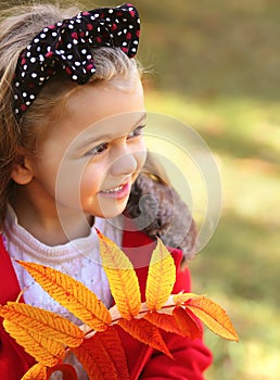 Portrait macro happy child with autumn leaves in the park. A little girl with a black polka dot bow headband and long curly blond