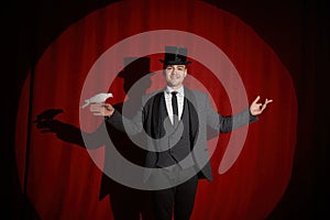 Portrait of magician with pigeon standing over red drapery in spotlight