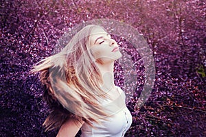 Portrait of magnificent woman with blowing hair on blossom purple flowers background