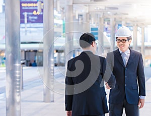 Portrait of male architect with safety hardhat greeting his partner. Young man builder showing handshake. Partnership concept.team