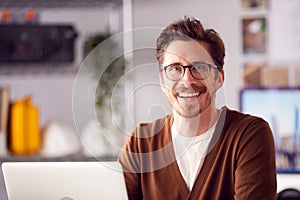 Portrait Of Male Architect Sitting At Desk In Office Working On Laptop