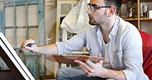 Portrait Of Male Artist Working On Painting In Studio