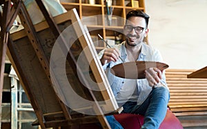 Portrait Of Male Artist Working On Painting In Studio