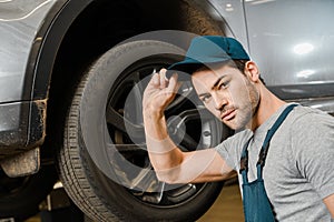 portrait of male auto mechanic in working overall posing near car