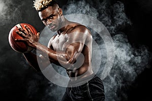 Portrait of afro-american sportsman, basketball player with a ball over black background. Fit young man in sportswear