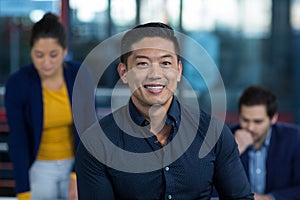 Portrait of male business executive smiling with colleague working in background