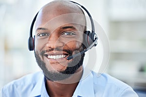 Portrait of male call center agent with a headset working in a corporate office doing crm. Cheerful, young and African