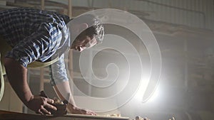 Portrait male carpenter in shirt in dark workshop planing wood