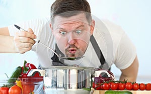 Portrait of male chef preparing and tasting hot food in vegetable soup spoon