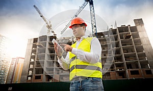 Portrait of male construction engineer standing on building site and using digital tablet