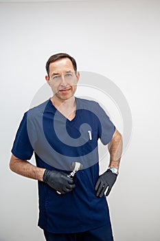 portrait of a male cosmetologist doctor in a blue medical uniform and black gloves with a dermatoscope in his hands.