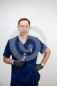 portrait of a male cosmetologist doctor in a blue medical uniform and black gloves with a dermatoscope in his hands.