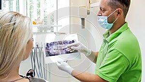 Portrait of male dentist talking to his patient and showing x-ray image