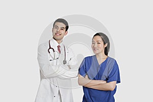 Portrait of male doctor and female nurse standing with hands folded over gray background