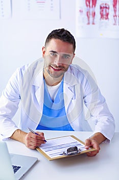 Portrait of a male doctor with laptop sitting at desk in medical office.
