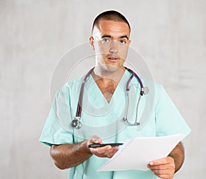 Portrait of male doctor in medical gown with stethoscope making notes in patient medical history