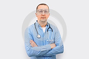 Portrait of a male doctor posing with crossed arms and looking at the camera on a light background.