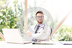 Confident male doctor portrait while sitting at desk photo