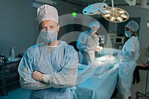Portrait of male doctor in surgical uniforms and masks standing posing looking at camera with crossed arms in operating