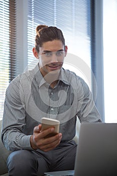 Portrait of male executive holding mobile phone while using laptop