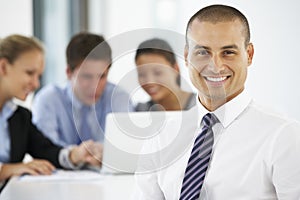 Portrait Of Male Executive With Office Meeting In Background photo