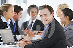 Portrait Of Male Executive With Office Meeting In Background