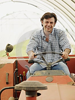 Portrait Of Male Farmer Driving Farm Tractor And Smiling