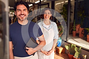 Portrait Of Male And Female Owners Of Florists With Digital Tablet Standing In Doorway With Plants