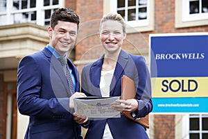 Portrait Of Male And Female Realtors Standing Outside Residential Property photo