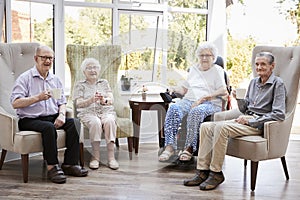 Portrait Of Male And Female Residents Sitting In Chairs In Lounge Of Retirement Home