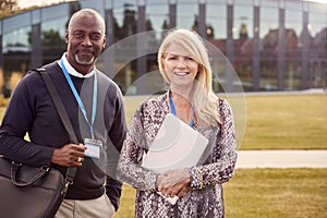 Portrait Of Male And Female University Or College Tutor Outdoors With Campus Building In Background