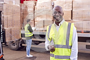 Portrait Of Male Freight Haulage Manager Standing By Truck Being Loaded By Fork Lift 