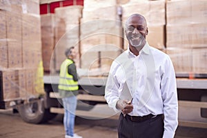 Portrait Of Male Freight Haulage Manager Standing By Truck Being Loaded By Fork Lift 