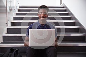 Portrait Of Male High School Student Sitting On Staircase And Using Laptop