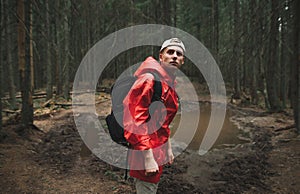Portrait of a male hiker in a red jacket feeling calm and relaxed in the fir forest. Young tourist man backpacker with serious