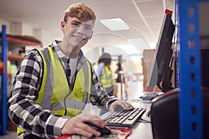 Portrait Of Male Intern Working In Busy Modern Warehouse On Computer Terminal