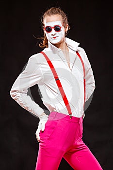 Portrait of male mime artist, isolated on black background. Man in suspenders and pink trousers is posing pointing with