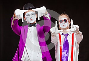 Portrait of male mime artists, isolated on black background. Two men wearing bright purple and pink suits gesticulate