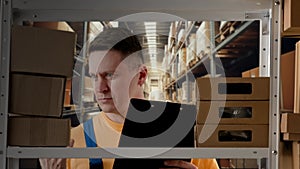 Portrait of male model working in storage. Man storekeeper standing near rack with boxes, checking goods, writing in