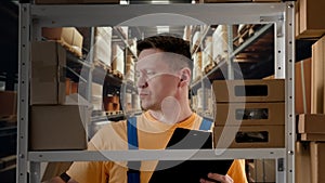 Portrait of male model working in storage. Man storekeeper standing near rack with boxes, taking package checking it and