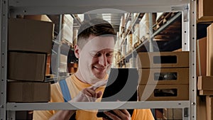 Portrait of male model working in storage. Man storekeeper standing near rack with boxes, watching social media on