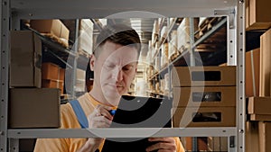 Portrait of male model working in storage. Man storekeeper standing near rack with boxes, watching social media on